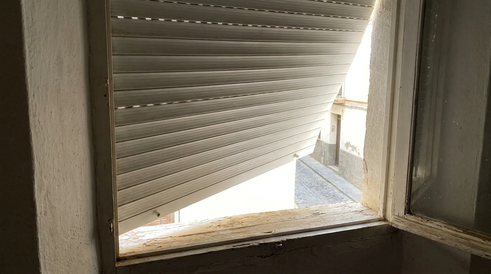 Persiana de aluminio atascada a media altura con las lamas torcidas en la guía de la ventana